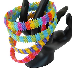 May include: Four colorful beaded bracelets stacked on a black display stand. The bracelets are made of small, square beads in shades of pink, purple, yellow, orange, green, and blue.