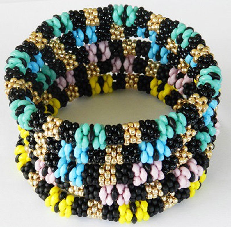Op de afbeelding: Meerkleurig kralenarmband met zwarte, turquoise, gele en roze kralen. De armband is gemaakt van meerdere rijen kralen en heeft een geweven patroon.