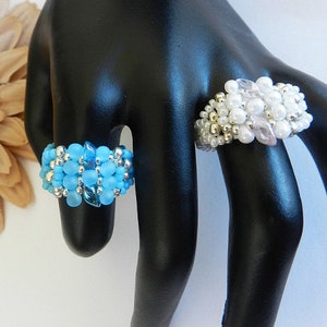 May include: Two beaded rings on a black ring display stand. The ring on the left is blue and silver. The ring on the right is white and silver.