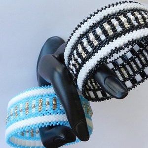 Op de afbeelding: Twee kralenarmbanden, een zwart-wit, de andere blauw, wit en goud, op een zwarte mannequinhand.