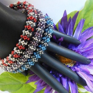 May include: Four beaded bracelets stacked on a black mannequin hand. The bracelets are made of silver, red, blue, and purple beads. The bracelets are on a background of a purple flower.