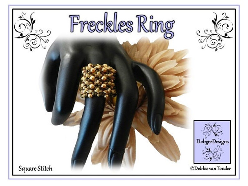 K&ouml;nnte beinhalten: Ein goldfarbener und brauner Perlenring, genannt "Freckles Ring", wird auf einem schwarzen Handmodell gezeigt. Der Ring ist mit quadratischem Stich gefertigt. Das Bild tr&auml;gt den Titel "Freckles Ring" und enth&auml;lt den Text "DebbiegerDesigns" und "Debbie van Tonder".