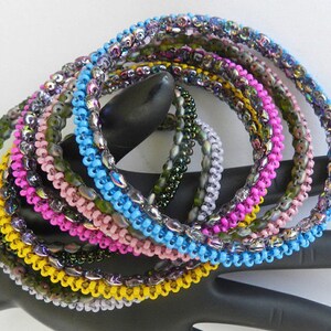 May include: A set of eight beaded bracelets in various colors, including yellow, pink, blue, and green. The bracelets are made of small, iridescent beads and are stacked on top of each other.