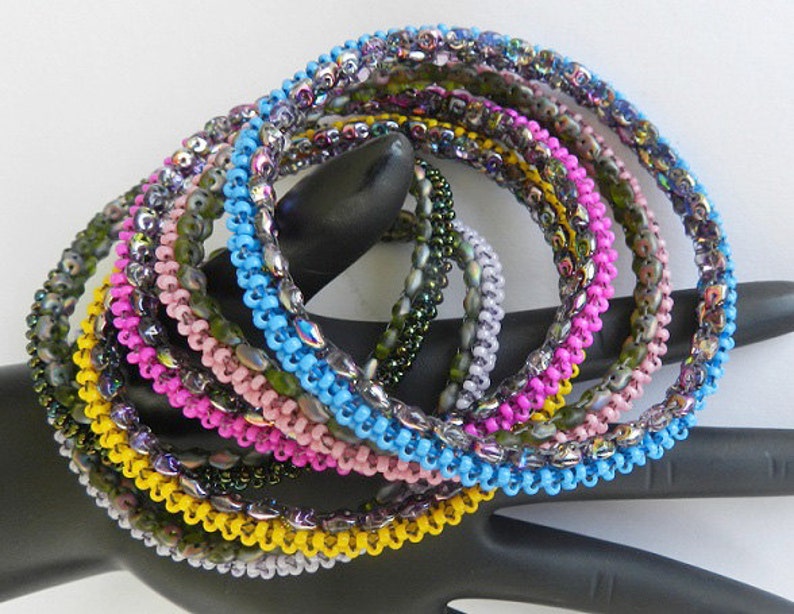 May include: A set of eight beaded bracelets in various colors, including yellow, pink, blue, and green. The bracelets are made of small, iridescent beads and are stacked on top of each other.