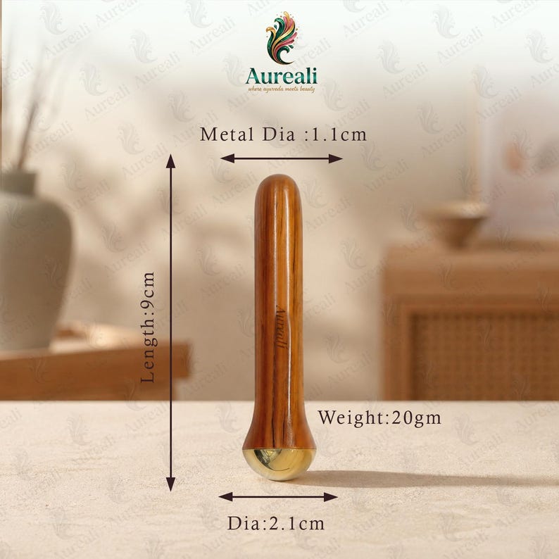 Puede incluir: Una herramienta de masaje de madera con base dorada y parte superior redondeada. La herramienta mide 9 cm de largo, con un di&aacute;metro de 2,1 cm en la base y un di&aacute;metro met&aacute;lico de 1,1 cm. Pesa 20 g. La marca "Aureali" es visible.