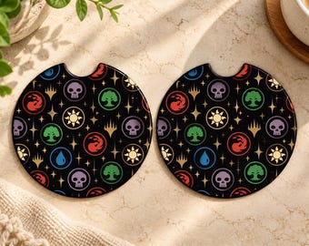 Peut inclure: Deux sous-verres de voiture circulaires avec un fond noir et un motif répétitif de symboles de mana Magic: The Gathering colorés, incluant des crânes, des arbres, des soleils, des flammes et des gouttes d'eau, parsemés de petites étoiles dorées.
