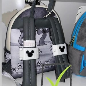 Puede incluir: Una mochila gris y blanca con un diseño de dibujos animados espeluznante con esqueletos y árboles. La mochila tiene correas grises y detalles en blanco, con un logotipo de Mickey Mouse en los soportes de las correas. La mochila está en un estante blanco.