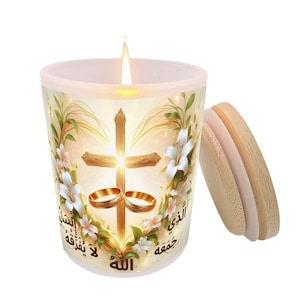 May include: A lit candle in a glass jar with a wooden lid. The jar is decorated with a cross, wedding rings, and floral elements. Arabic text is visible on the jar. The candle is designed for religious or wedding ceremonies.