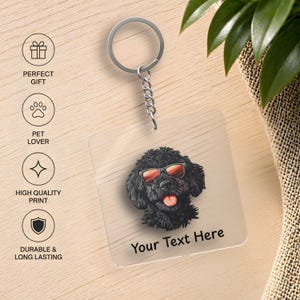 May include: A clear acrylic keychain with a silver keyring and chain. The keychain features a black dog wearing sunglasses with a red tint and the text "Your Text Here". The keychain is a pet lover gift.