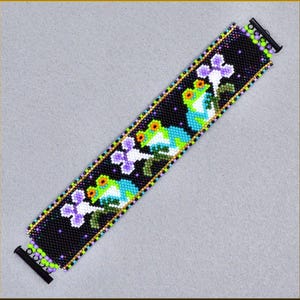 May include: A beaded bracelet featuring a repeating pattern of green and blue frogs with orange accents, and purple and white flowers, set against a black background. The bracelet has a gold border and black clasp.
