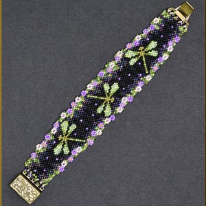May include: A beaded bracelet with a black background, featuring a dragonfly design in green and yellow. The bracelet is adorned with purple and white floral accents and has a gold-colored clasp.