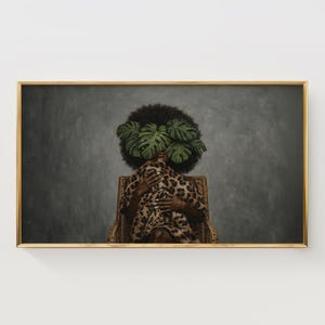 Puede incluir: Impresión artística enmarcada. Una persona con afro tiene hojas verdes que le cubren la cara. Viste una prenda con estampado de leopardo y está sentada en una silla de mimbre. El fondo es gris y el marco es dorado.