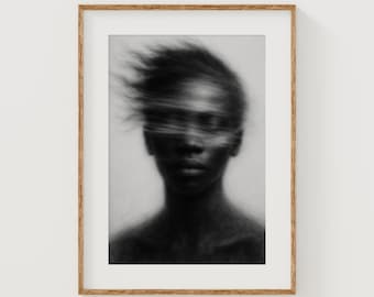 May include: A framed black and white portrait of a person with blurred facial features and flowing hair. The artwork is presented in a wooden frame, creating a minimalist aesthetic. The image is a study in contrasts, with soft shading and a focus on form.