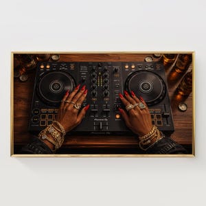 May include: A framed image of a DJ setup with hands adorned with gold jewelry and red nail polish. The DJ mixer is black with silver accents. Bottles and bottle caps are visible on the wooden surface.