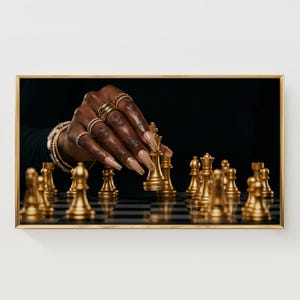 Könnte beinhalten: Gerahmtes Foto eines Schachspiels im Gange. Eine Hand mit langen, goldfarbenen Nägeln und mehreren Ringen bewegt eine goldene Schachfigur auf einem schwarz-weiß karierten Brett. Die Schachfiguren sind goldfarben.