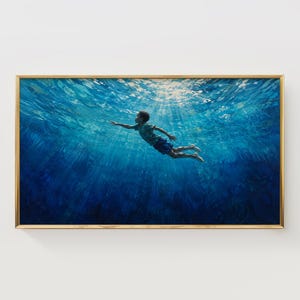 May include: A framed horizontal wall art print depicting a person swimming underwater in deep blue water. Sunlight filters through the surface, creating bright rays and ripples above. The swimmer wears a green shirt and dark blue shorts.