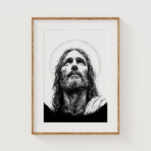 May include: Black and white portrait print of a man with long hair and a beard, looking upwards. A halo of light surrounds his head. The artwork is framed in a wooden frame.