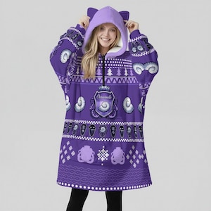 May include: A purple hooded blanket with a zip-up front and cat ears on the hood. The blanket features a repeating pattern of white seashells, coffins, and the text "Octavinelle" on the front.