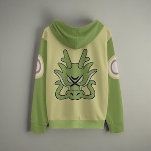 Puede incluir: Sudadera con capucha verde con un gráfico de dragón amarillo en la espalda. El dragón tiene un cuerpo verde y un círculo rosa en cada manga.