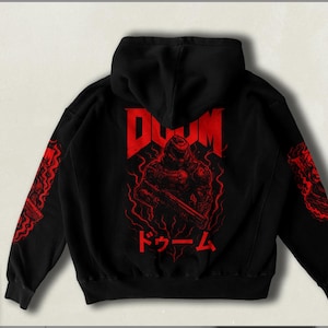 Könnte beinhalten: Schwarzer Kapuzenpullover mit einem roten Grafikdruck eines Dämons, der eine Waffe hält. Der Text "DOOM" und "ド-ム" ist in Rot auf dem Pullover gedruckt.