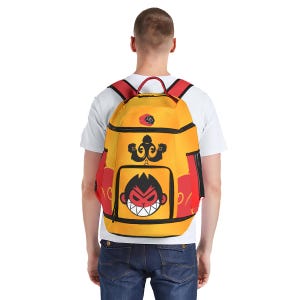 May include: Yellow and red backpack with a cartoon devil face design on the front. The backpack has black trim, red shoulder straps, and a red top handle. The design includes a black emblem and a cartoon devil face with a white grin.