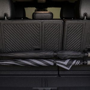 Puede incluir: Dos paraguas se guardan en la parte trasera de un vehículo. Uno es negro liso y el otro es de rayas negras y grises. Los paraguas están asegurados en un compartimento de almacenamiento, con los mangos visibles.