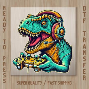 May include: A DTF transfer featuring a teal and orange Tyrannosaurus Rex wearing headphones with a microphone, holding a yellow game controller. The text READY TO PRESS is on the left, DTF TRANSFER on the right, and SUPER QUALITY FAST SHIPPING below.