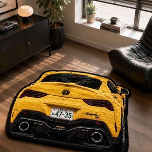 May include: Yellow and black car-shaped rug. The rug features the rear of a sports car, with details including taillights, exhaust pipes, and a license plate. The rug is placed on a wooden floor.