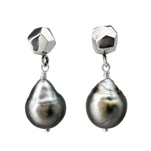 May include: A pair of silver earrings with a geometric top and a large, teardrop-shaped, dark gray pearl. The pearls have a lustrous, iridescent sheen. The earrings are suspended by a delicate silver wire.