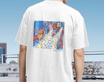 May include: White t-shirt featuring a colorful illustration of Times Square, with yellow taxis and bustling crowds. The artwork includes vibrant buildings and billboards, with the words "times square" at the bottom.
