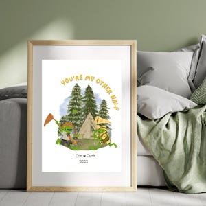 Op de afbeelding: Een digitale illustratie van twee kikkers die kamperen in het bos. De tekst "You're my other half" staat in een cirkel rond de kikkers. De kikkers houden kampeeruitrusting vast en er is een tent en een kampvuur op de achtergrond. De tekst "Tom & Dash 2022" staat onder de kikkers.