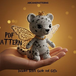 Könnte beinhalten: Ein gehäkeltes Leopardenjunges mit goldener Krone und Feenflügeln. Das Junge hat schwarze Flecken und trägt eine goldene Halskette. Das Bild enthält den Text "PDF PATTERN" und "Included Stitch Guide and Gifts".