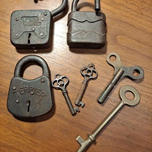 May include: Four antique padlocks and four keys. The padlocks are made of metal and have a dark brown finish. The keys are made of brass and have intricate designs. The padlocks are labeled "JULLER" and "TERRIER".