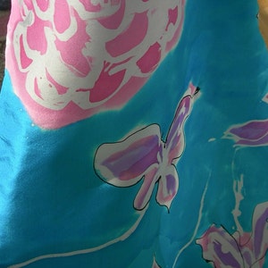 May include: A flowing fabric with a vibrant floral design. The fabric features large pink and white flowers and butterfly-like shapes against a bright turquoise background. The design is artistic and eye-catching.