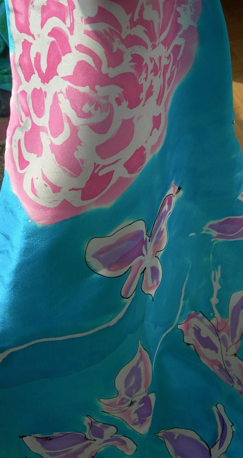 May include: A flowing fabric with a vibrant floral design. The fabric features large pink and white flowers and butterfly-like shapes against a bright turquoise background. The design is artistic and eye-catching.