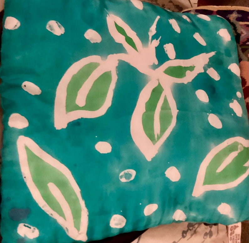 May include: Square decorative pillow with a teal background and a white and green leaf design. The leaves are outlined in white and filled with green. White polka dots are scattered across the pillow.