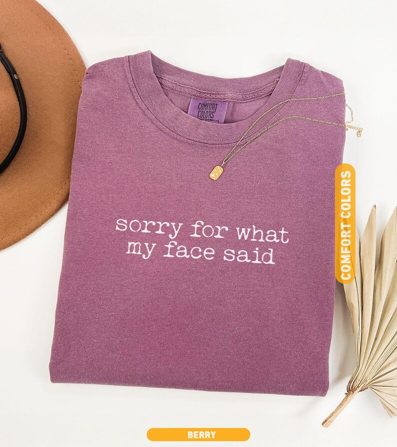 Pu&ograve; includere: T-shirt color bacca con la scritta bianca "sorry for what my face said". Una collana d'oro con un ciondolo rettangolare &egrave; appoggiata sulla maglietta. La maglietta &egrave; etichettata "Comfort Colors".