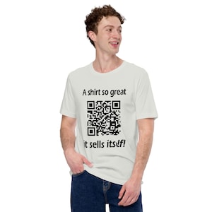 Peut inclure: Un t-shirt blanc avec du texte noir qui dit "A shirt so great it sells itself!" et un code QR noir.
