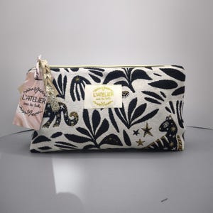 Pode incluir: Uma bolsa de cosm&eacute;ticos retangular com um padr&atilde;o de folhas em preto e branco. A bolsa tem um z&iacute;per dourado e uma etiqueta com o texto "L'ATELIER sous les toits". A bolsa &eacute; decorada com estrelas douradas e um animal preto e dourado.