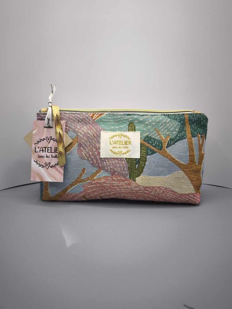 Pode incluir: Necessaire retangular de tape&ccedil;aria com um desenho de paisagem em tons de azul, verde, rosa e castanho. A bolsa tem um fecho de correr dourado e uma etiqueta que diz "L'ATELIER sous les toits".