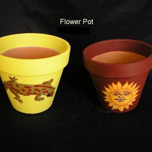 May include: Two terracotta flower pots, one yellow with a red and brown gecko painted on it, and the other brown with a yellow sun with a face painted on it.