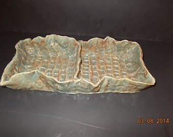 May include: A ceramic serving dish with two sections. The dish is a light blue-green color with a textured surface. The dish has a unique, organic shape.