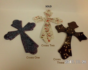 May include: Three ceramic crosses with different paint splatters. The cross on the left is purple with blue splatter, the middle cross is white with red splatter, and the cross on the right is brown with gold splatter. The text "Cross One", "Cross Two", and "Cross Three" is written below each cross. The text "SOLD" is at the top of the image. The date "2011.11.26" is at the bottom right of the image.