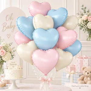 May include: A cluster of heart-shaped foil balloons in pastel pink, light blue, and cream colors. The balloons are tied together with white ribbons and a light pink satin bow at the base, creating a decorative arrangement for a celebration.