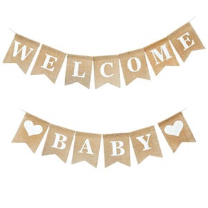 May include: Two burlap banners with white text and heart shapes. The top banner reads "WELCOME" and the bottom banner reads "BABY". The banners are strung together with thin white string, perfect for a baby shower.