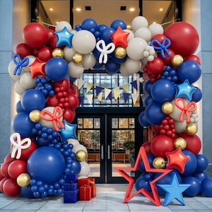 May include: A festive balloon arch in red, white, and blue, with star and bow accents. The arch frames a doorway, with gift boxes at the base. Gold and blue star-shaped balloons add to the celebratory decor.