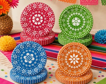 May include: Four stacks of round paper plates in red, green, blue, and orange, each featuring a white floral mandala pattern. The plates are arranged on a colorful striped runner, accompanied by paper flowers and confetti decorations.