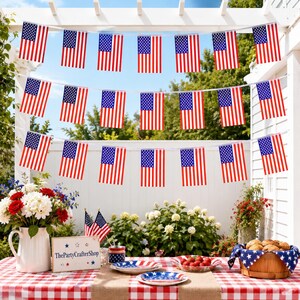 May include: A festive outdoor scene with American flag bunting strung across a white pergola. A table is set with red and white checkered tablecloth, plates, and a basket of bread. Flowers and strawberries add color to the patriotic display.