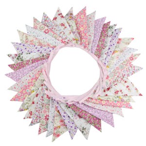 May include: A floral fabric bunting in a circular arrangement. The pennants feature various floral patterns in shades of pink, purple, and white. A pink ribbon forms the circle's base, creating a decorative wreath-like design.