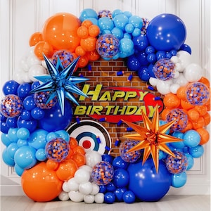 May include: A festive birthday balloon arch in shades of blue, orange, and white. The arrangement includes star-shaped decorations and confetti-filled balloons. The words "HAPPY BIRTHDAY" are displayed on a brick-patterned backdrop.